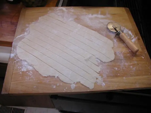 In the center of the image there is a dough on the wooden surface and there is also a making object...