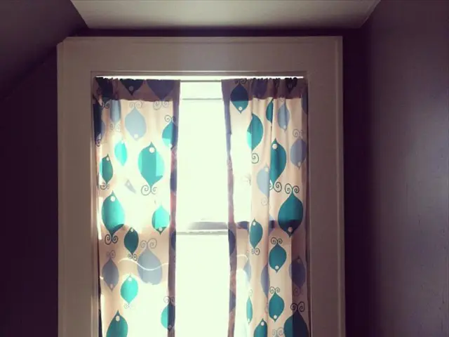 In the image there is a window in the middle with curtains on the wall.